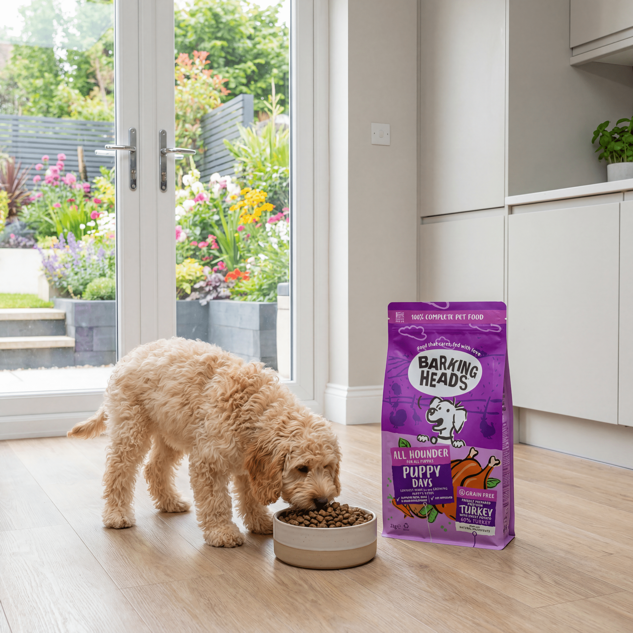 Small cockapoo puppy eating dog food from a bowl next to a bag of Barking Heads' puppy food